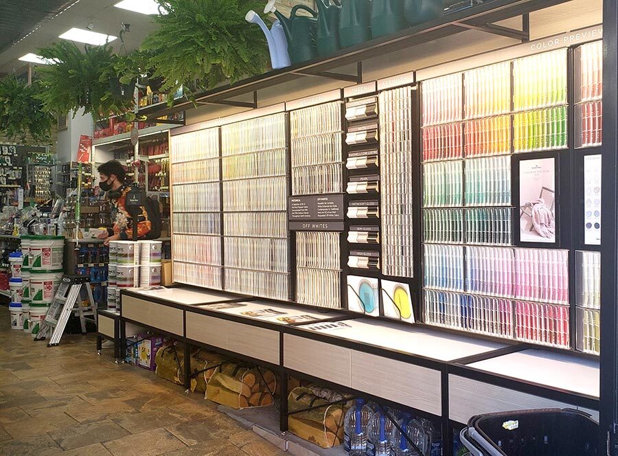 Space above the Benjamin Moore paint chip display is used to stock plants and watering cans, while below is used to merchandise firewood and cases of bottled water.